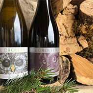 Two bottes of La Chouette wines in from of a stack of wood